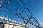 Barbed And Razor Wire On A Fence With A Security Camera In The Background